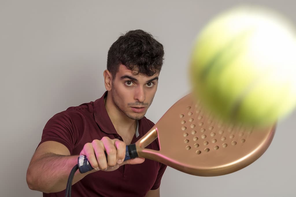 Young man holding Padel racket and hitting the ball in the studio